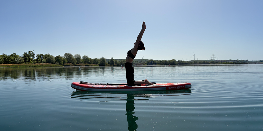 Frau in Yoga-Pose auf einem Stand-Up-Paddle auf dem Stotternheimer See
