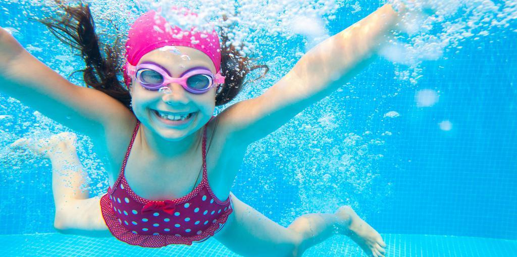 Mädchen mit Schwimmbrille und Badekappe schwimmt unter Wasser